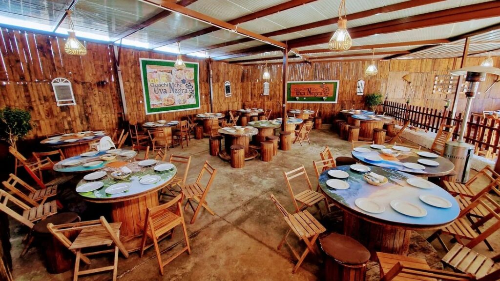 Rustic indoor dining area with round log tables, wooden chairs, and warm hanging lanterns.