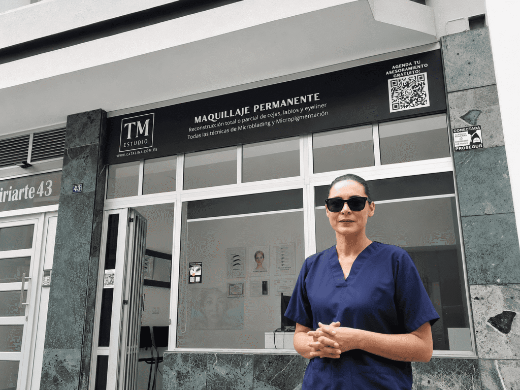 Woman in blue scrubs wearing sunglasses stands outside a beauty clinic offering permanent makeup.